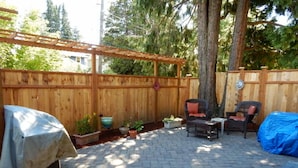 Eine Terrassenfläche mit Holzzaun, einer Pergola und Gartenmöbeln, darunter ein Tisch und Stühle mit Überdachung.