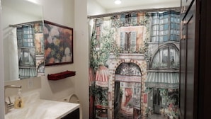 Ein Badezimmer mit großem Spiegel, Waschbecken und Toilette. An der Wand befindet sich ein Wandbild, das eine Straßenszene mit Gebäuden und einem Fahrrad zeigt.