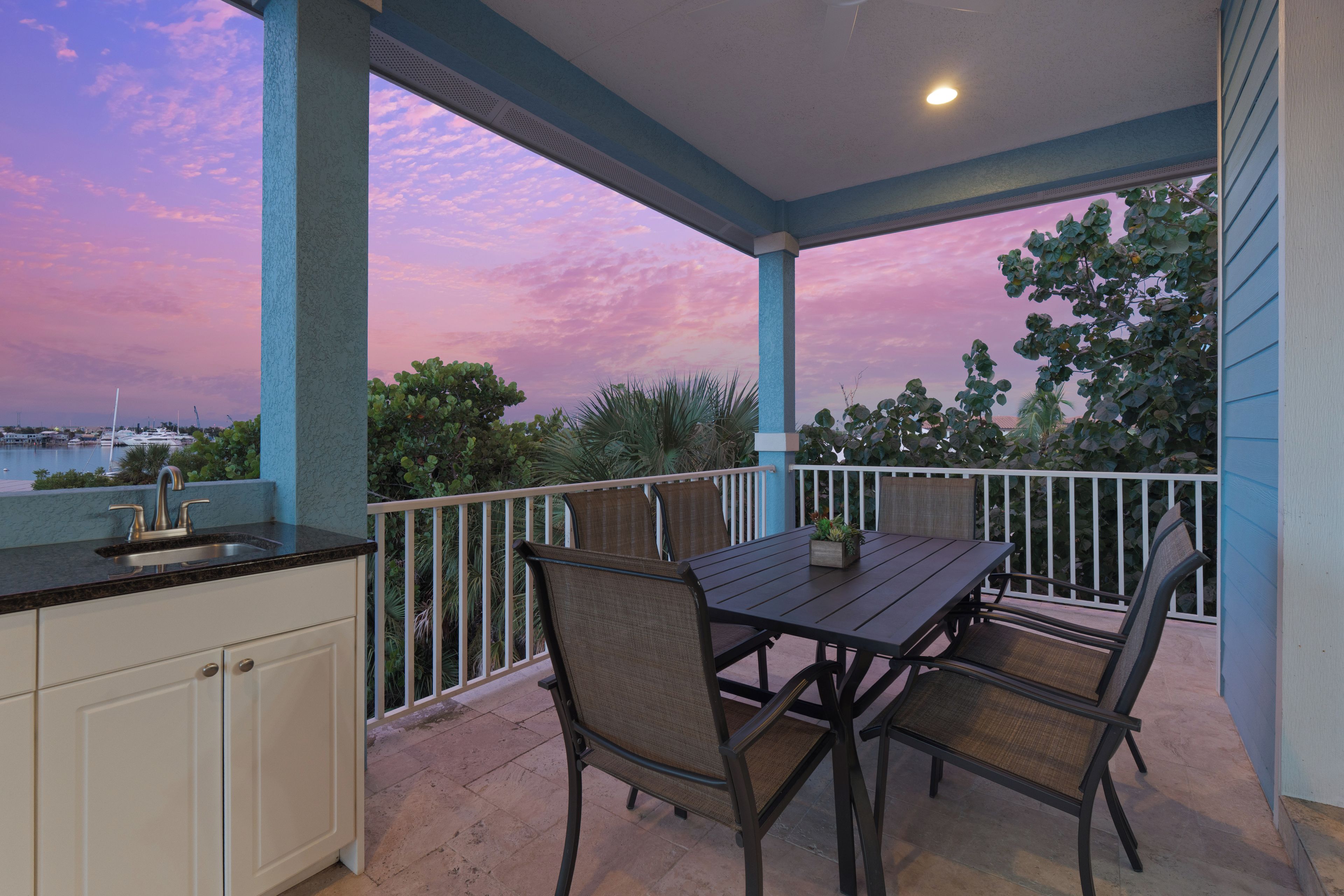 A covered outdoor area with a table and chairs, a sink, and a view of the water and boats.