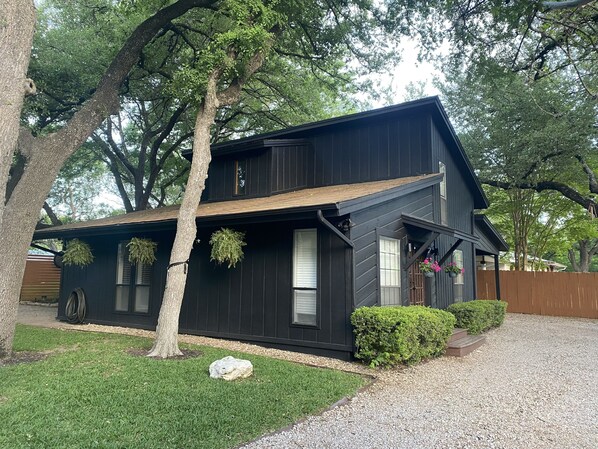 A two-story house with a dark exterior, a sloped roof, and a gravel driveway. - The Retreat (Austin)