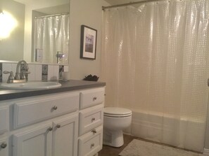 A bathroom with a sink, mirror, toilet, and shower curtain. - The Retreat (Austin)