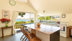 Una cocina con una isla grande, sillas de madera, vista al mar y un reloj en la pared.