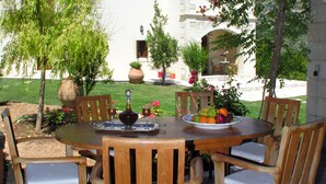 Eine Terrasse im Freien mit einem runden Holztisch, sechs Holzstühlen und einer Obstplatte.