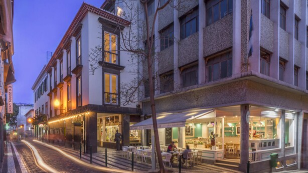 A street view of a building with multiple ground-floor shops and cafes, featuring outdoor seating and a visible restaurant interior. - Downtown Funchal Apartments 1C Cedros. (Funchal)