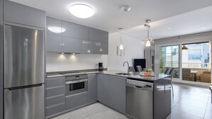 A modern kitchen with stainless steel appliances, grey cabinetry, and a large window providing a view of the outdoors.