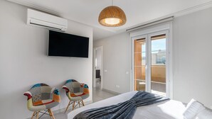 A modern hotel room with a bed, two colorful chairs, a flat-screen TV, and a large window with a view of the outside.