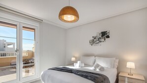 A bedroom with a bed, bedside lamps, a wall art piece, and a sliding glass door to a balcony.