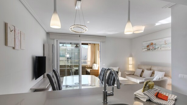 A modern kitchen with a central island, a dining area with chairs, a sofa, and a TV mounted on the wall.