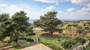 A garden with stone walls, trees, and a view of the sea.