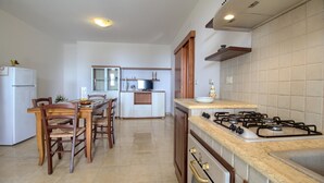 A kitchen with a gas stove, a refrigerator, a dining table with chairs, and a window.