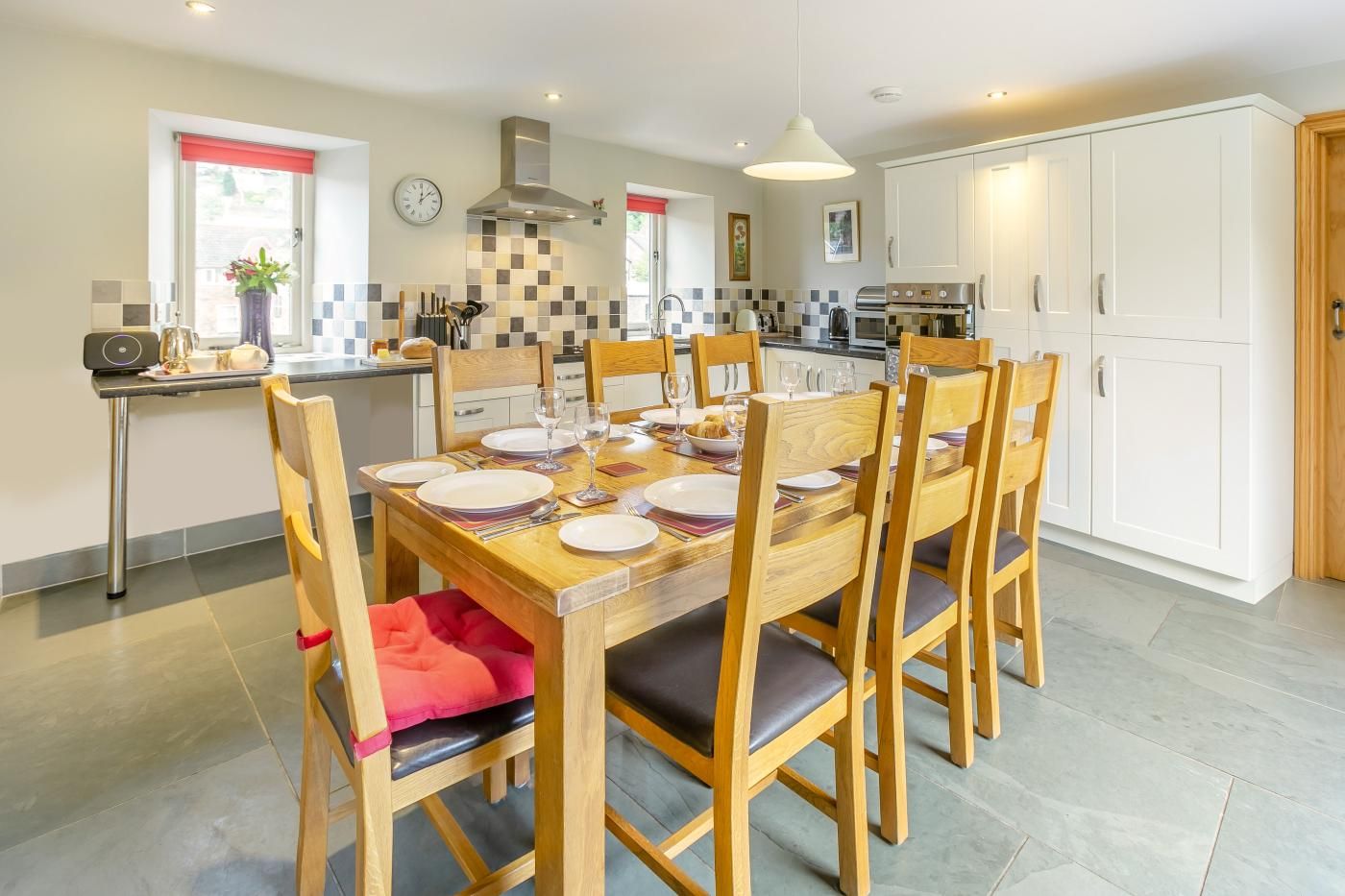 Een moderne keuken met witte kasten, een roestvrijstalen afzuigkap en een eethoek met houten stoelen en een tafel gedekt voor vier personen.
