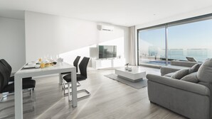 Una sala moderna con comedor, televisor de pantalla plana y un gran ventanal corredero que da a un balcón con vista a la piscina.