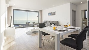Habitación de hotel moderna con comedor, sofá y un amplio ventanal con vistas al cielo.