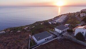 Un área residencial costera con casas modernas, una vista despejada del mar y un atardecer al fondo.