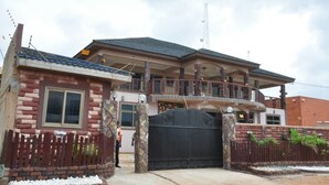 A two-story house with a balcony, a gated entrance, and a stone facade. - Villa D' Coco (Accra)