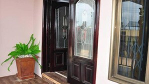 A dark wooden door with a glass panel, a potted plant, and a window with a lattice design. - Villa D' Coco (Accra)