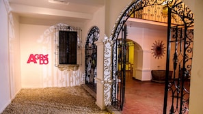 A hallway with a decorative iron gate, a window with a metal grille, and a wall with a logo. - Agrado Guest House (Oaxaca)