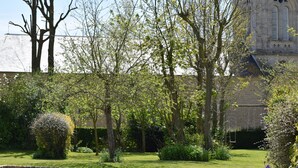Un jardin avec une pelouse, des arbres et un bâtiment doté d’une façade en pierre.
