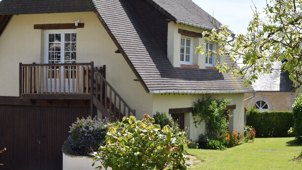 Une maison à deux étages, dotée d’un toit à forte pente, d’une terrasse en bois et d’un jardin bien entretenu.