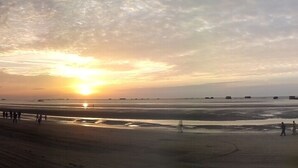 Une plage au coucher du soleil, avec un rivage sablonneux et quelques personnes qui se promènent.