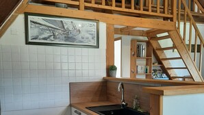 Une cuisine avec un escalier en bois, un évier, une cuisinière et un mur recouvert de carreaux.
