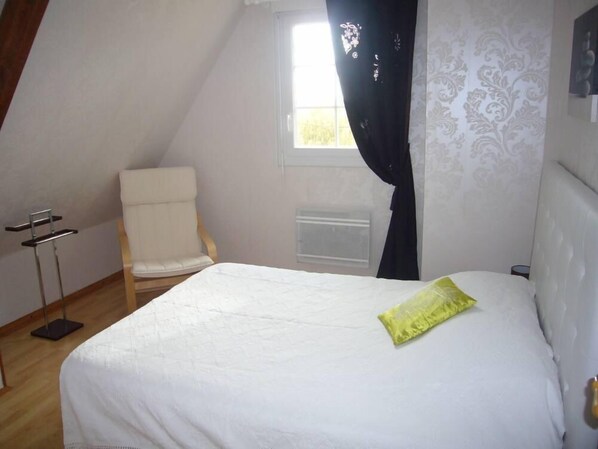 Une chambre à coucher avec un lit, une chaise, une fenêtre avec des rideaux et un radiateur.