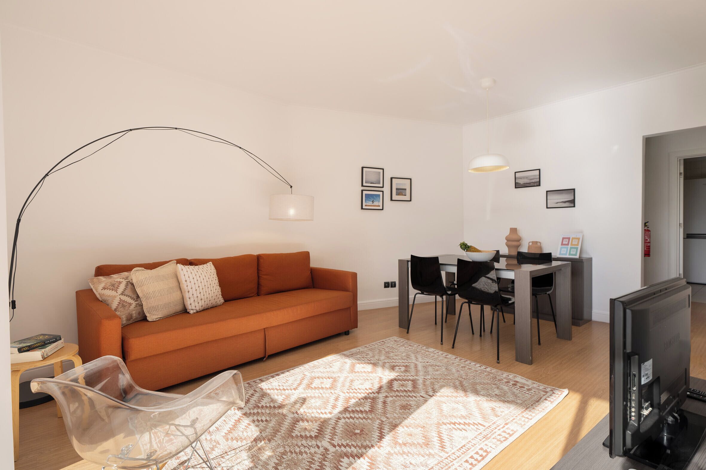 A modern living room with a sofa, a dining table, chairs, a TV, and a patterned rug.