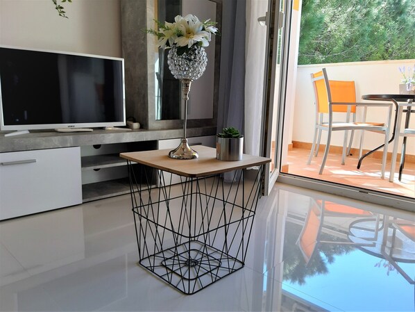 A modern living room with a flat-screen TV, a wooden coffee table, and a decorative vase with flowers.