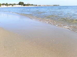 A beach with clear water, a sandy shore, and buildings in the background.
