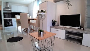 A modern kitchen with white cabinets, a built-in oven, a dining area with a table and chairs, a TV on a stand, and a decorative plant. - Apartment Kristina 400 m from the sandy beach + air condition + WiFi +dishwasher (Medulin)