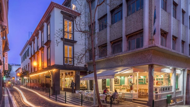 Una vista di una strada con un edificio che presenta un ristorante al piano terra, con posti a sedere all'aperto e un ingresso ben visibile.