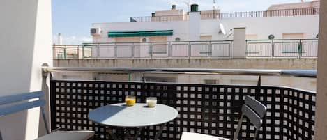A balcony with a table and two chairs, overlooking a building with a green awning and a fence.