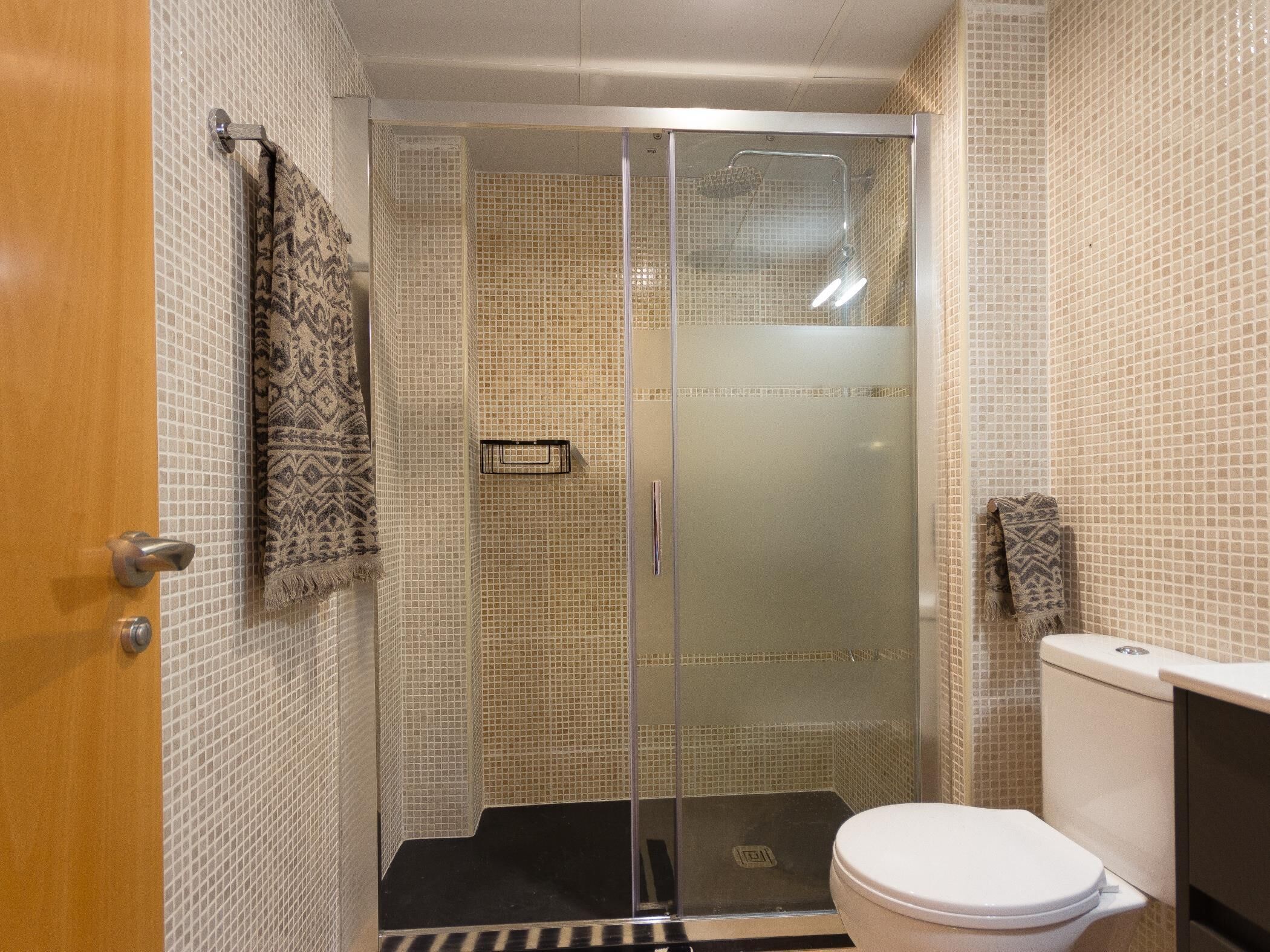 A bathroom with a glass shower enclosure, a toilet, and patterned tiles.