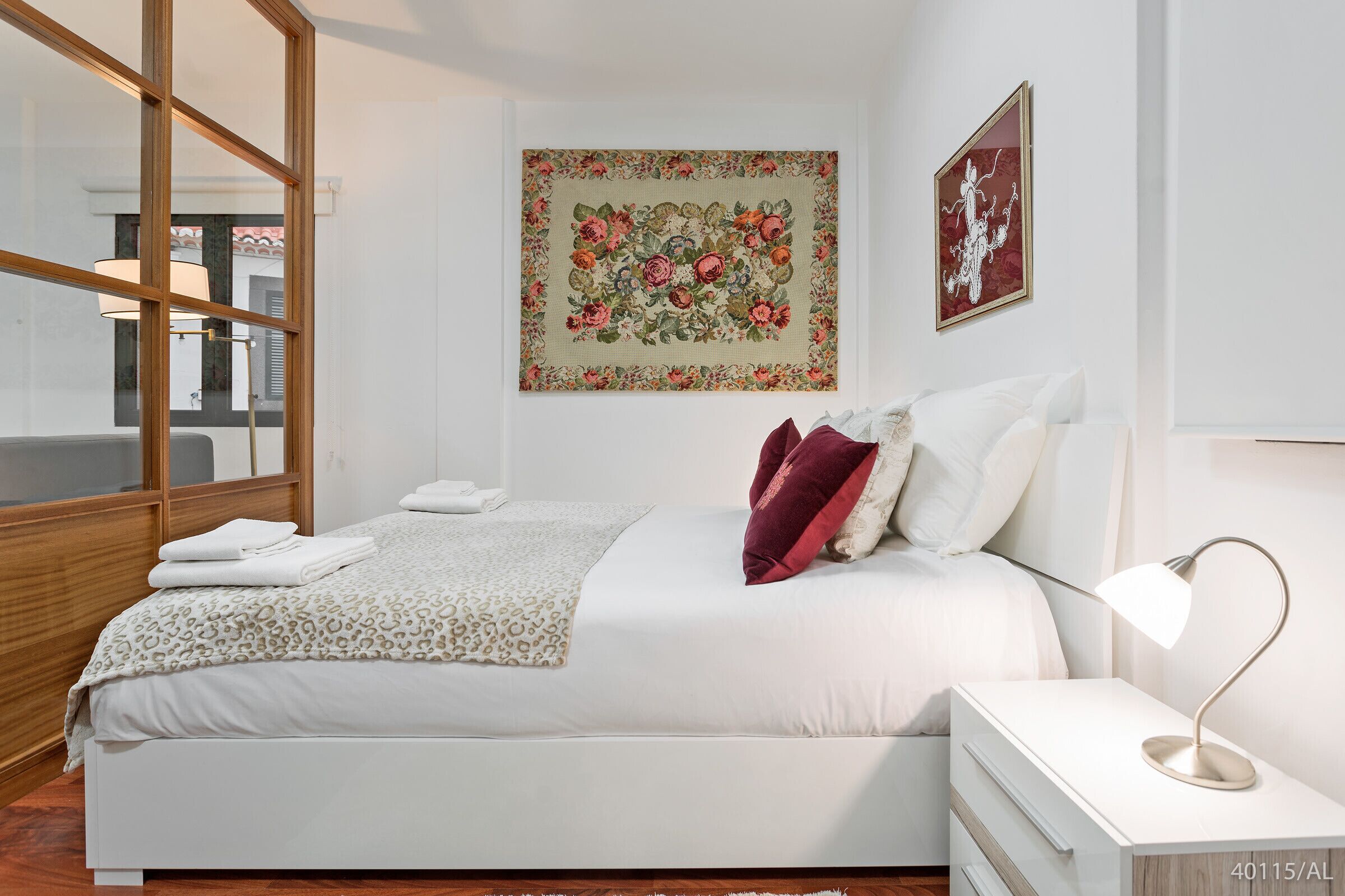 A neatly made bed with white linens and a leopard print throw, a bedside lamp, and a wall with two framed artworks.