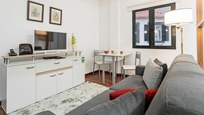 Ett modernt vardagsrum med en grå soffa, ett vitt TV-bord, ett matbord och en lampa.