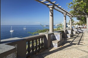 En utsikt över havet med en pergola, stentrappor och en klarblå himmel.