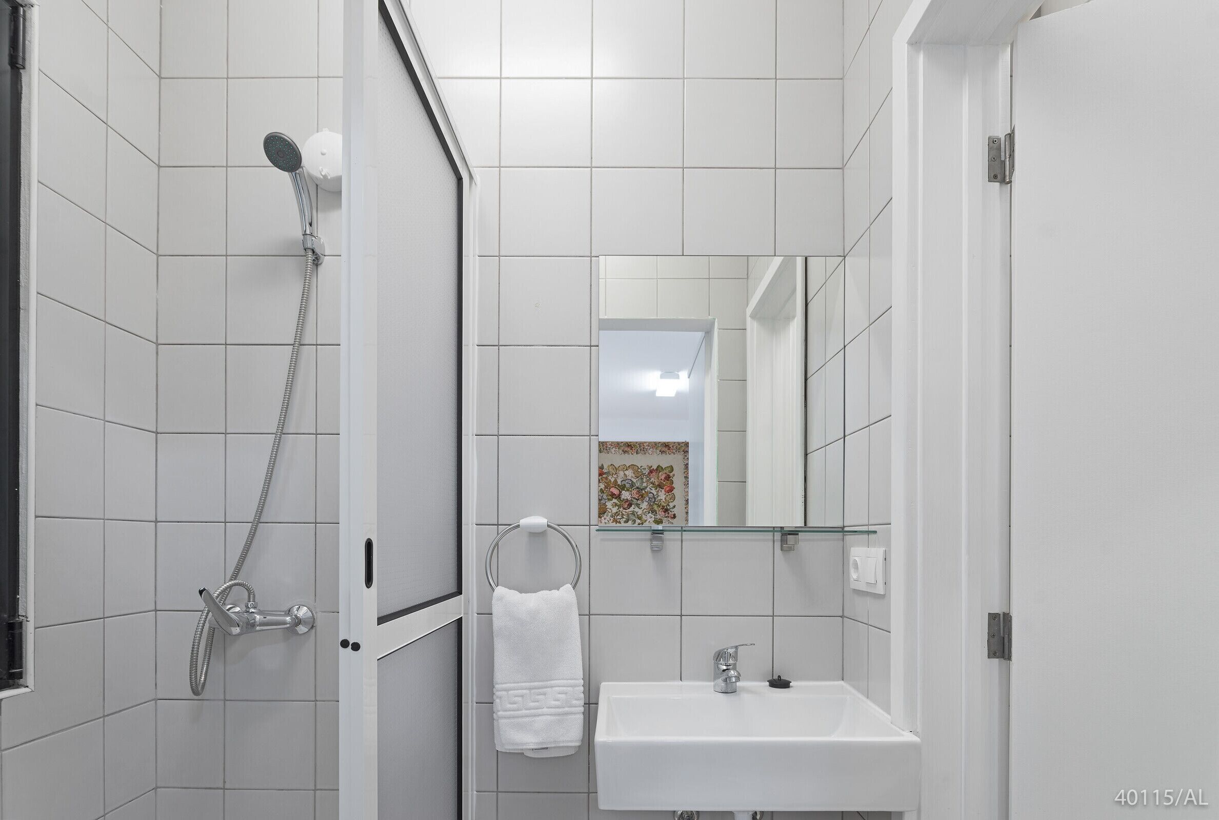 Ein modernes Badezimmer mit weißen Fliesen, einer Dusche, einem Waschbecken und einem Spiegel.