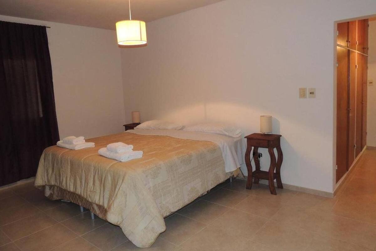 Een hotelkamer met een bed, nachtkastje met een lamp, een houten garderobe en een deur.