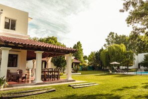 Una casa con porche techado, mobiliario exterior y piscina.
