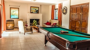Une salle de billard équipée d’une table de billard, de deux fauteuils, d’un canapé, d’une chemin ée et d’une porte en bois.
