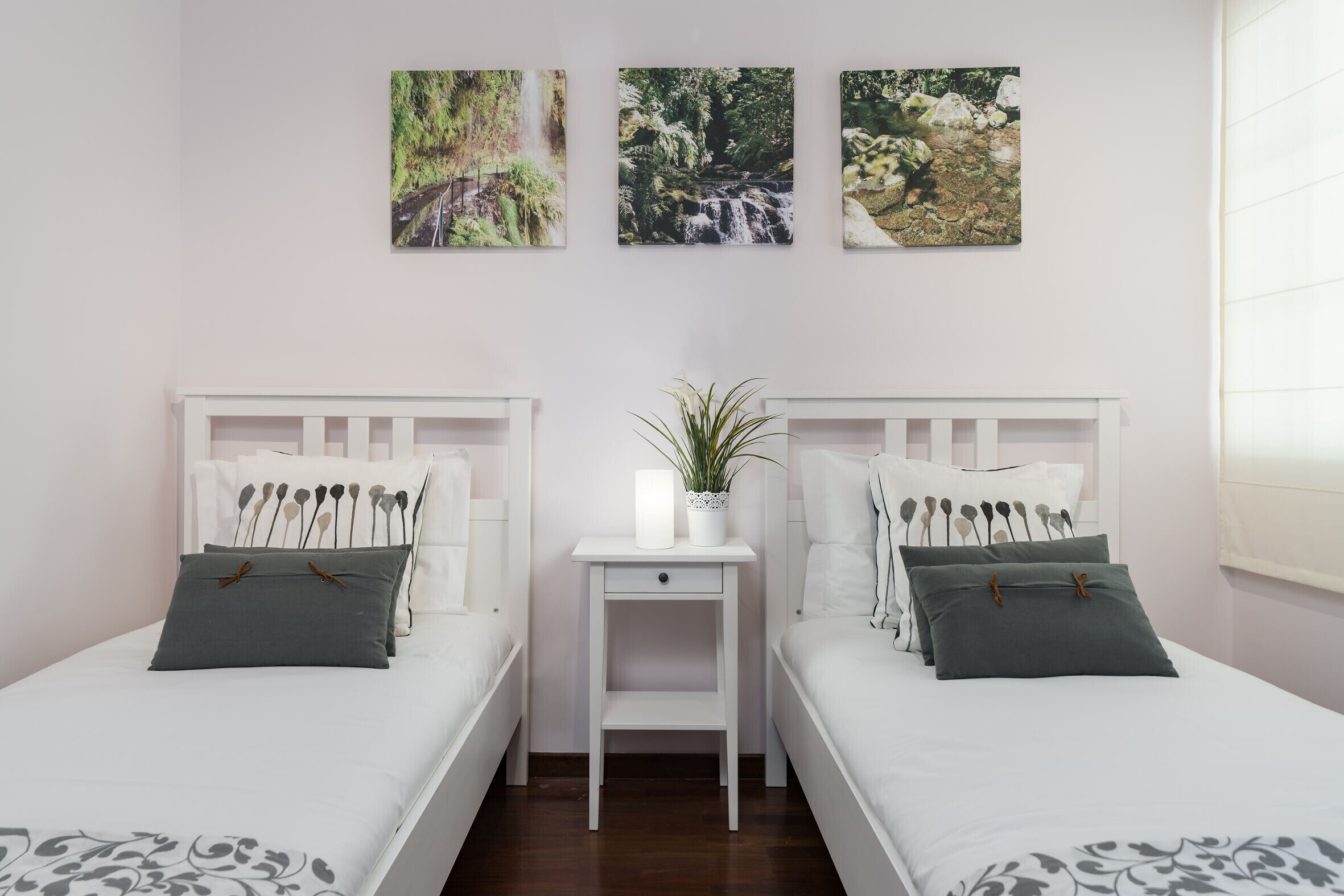 Une chambre avec deux lits, une petite table de chevet blanche agrémentée d’une plante, et trois œuvres d’art murales sur le thème de la nature.