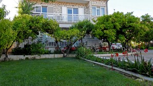 A two-story building with a stone facade, a balcony with white railings, and a well-maintained garden with various plants and flowers. - Cozy Apartment • Pool • close to Trogir & Airport (Trogir)