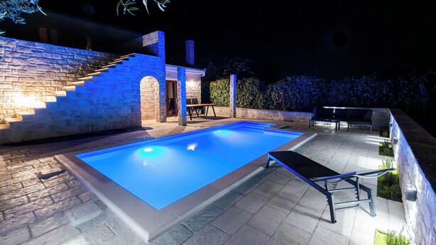A swimming pool with a stone deck and a staircase leading to a covered area. - Cozy Apartment • Pool • close to Trogir & Airport (Trogir)