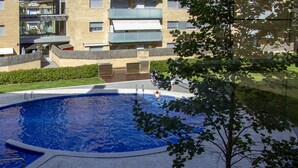 A swimming pool with a tiled deck, surrounded by a low brick wall and greenery.