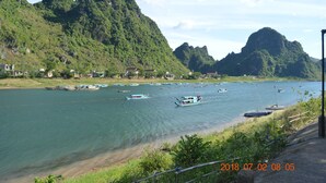 A river with boats, surrounded by green hills and houses. - Son Doong Riverside Homestay (Phong Nha)