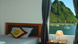 A hotel room with a bed, a nightstand with a lamp, and a view of boats on a lake with a mountain in the background. - Son Doong Riverside Homestay (Phong Nha)