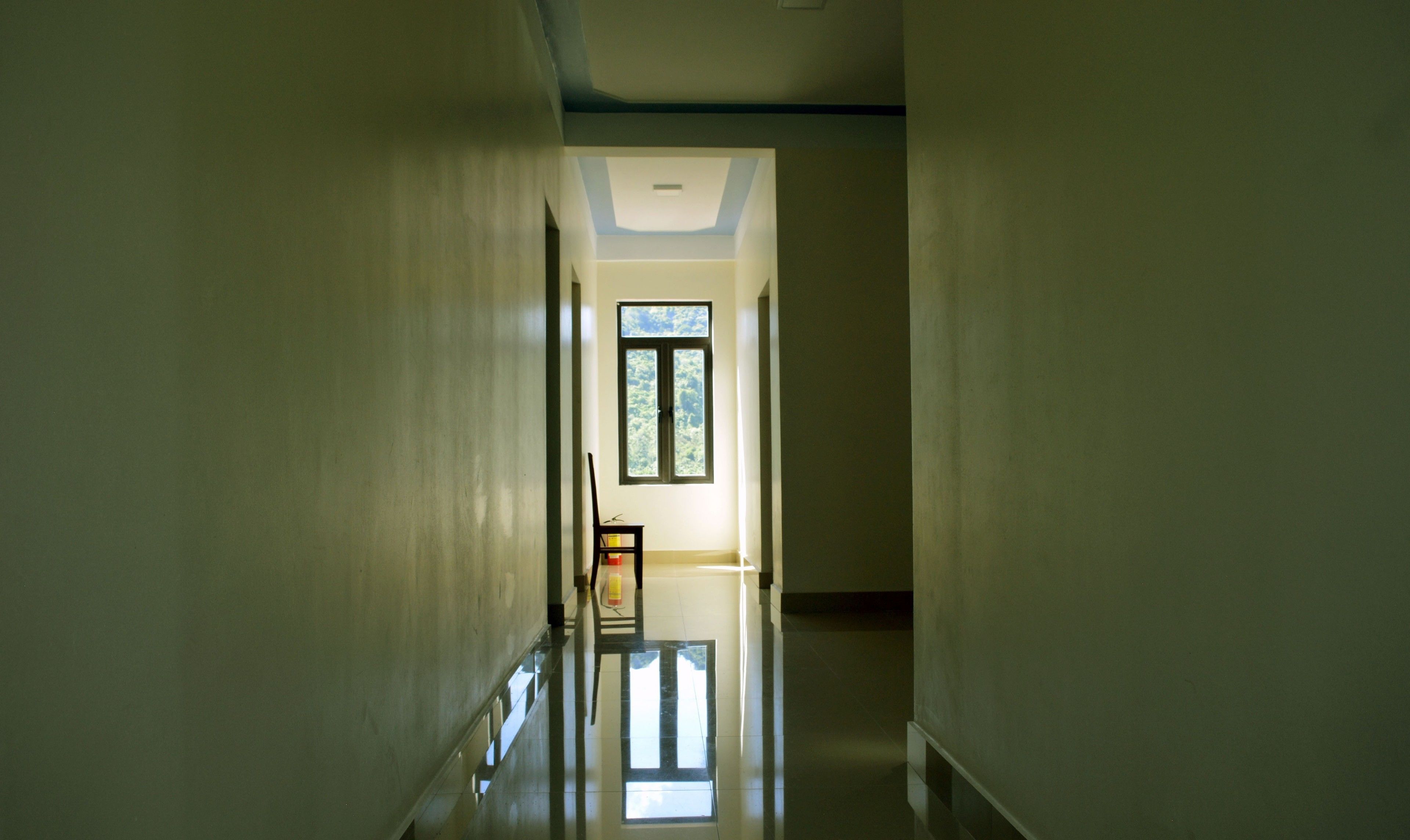A hallway with a skylight and a window, leading to a room with a chair and a table.