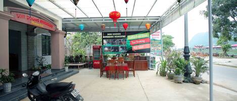 A covered area with a sign for Son Doong Riverside Homestay, a table and chairs, a parked motorcycle, and hanging lanterns.