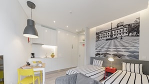 Una habitación de hotel moderna con zona de comedor, dos camas con ropa de cama a rayas, un sofá gris y un mural grande en la pared.