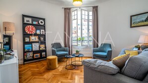 Een moderne woonkamer met een houten visgraatvloer, een zwarte boekenkast, twee blauwe fauteuils, een grijze bank en een gele hanglamp.